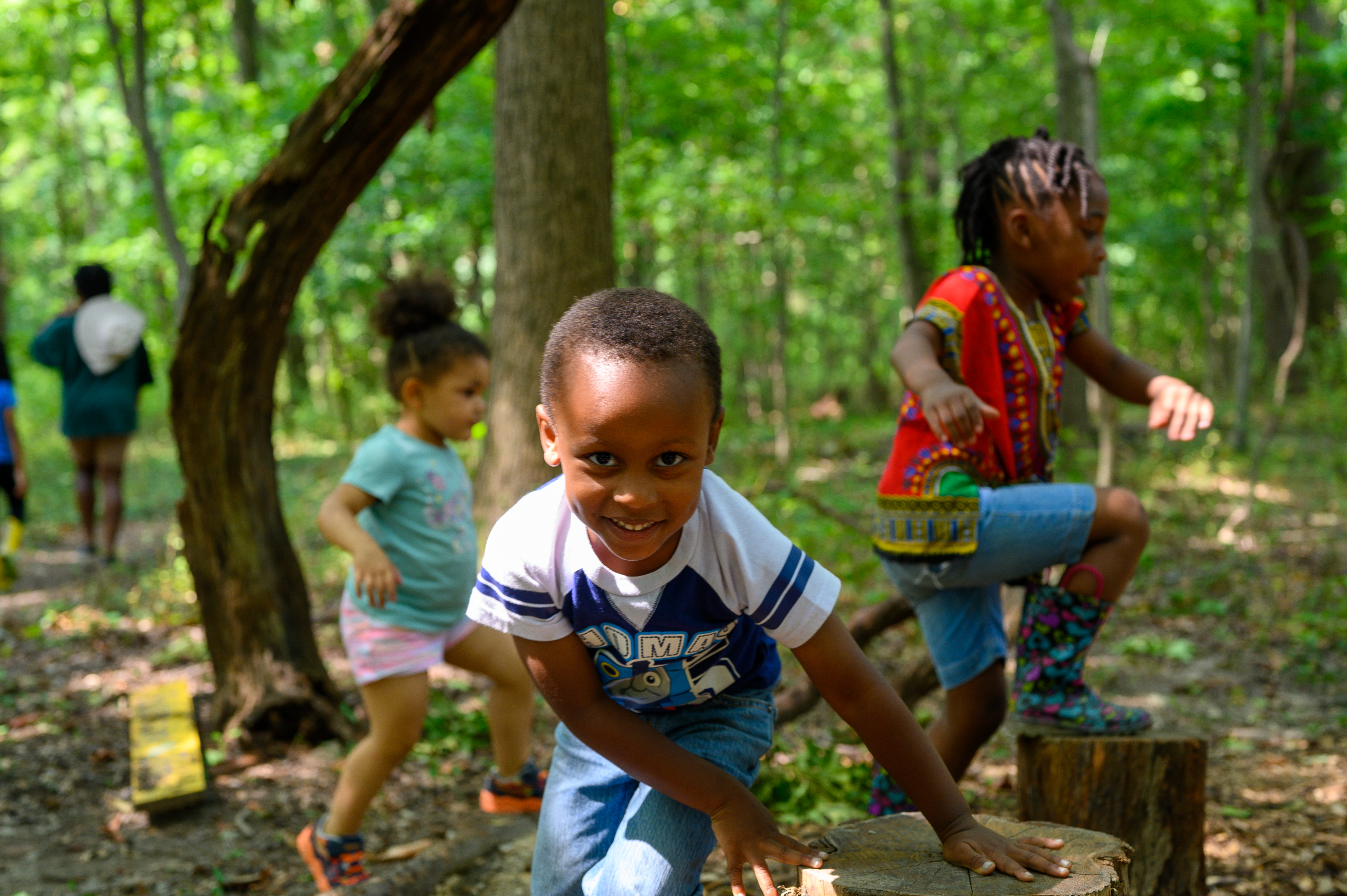 Young kids play in a forest, one of them looks into the camera while smiling